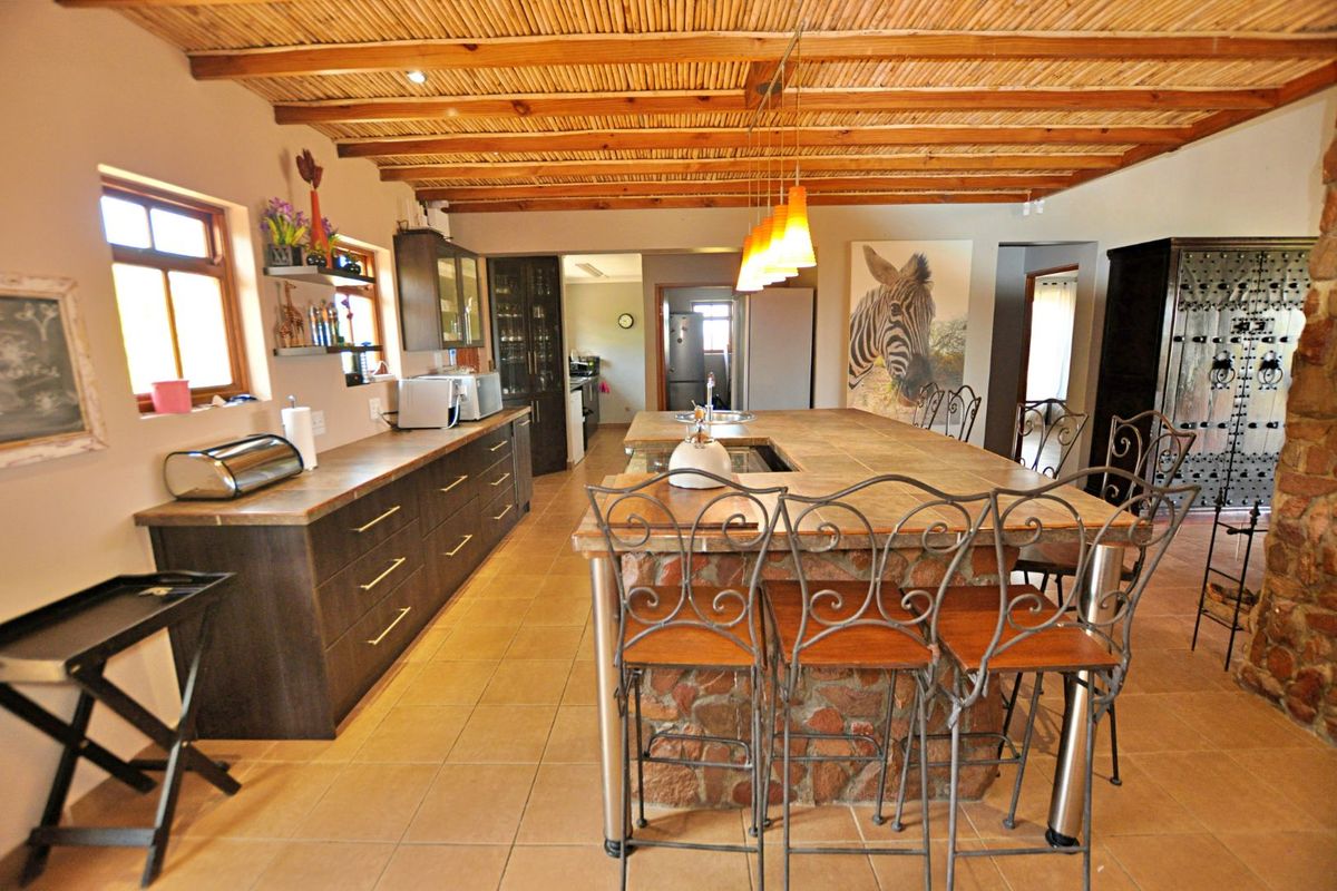 Spacious kitchen featuring a large stone-clad central island, dark cabinetry, tiled flooring, and a rustic exposed timber beam ceiling.