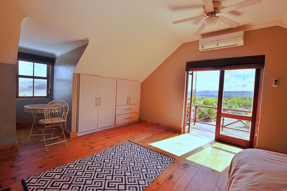 Spacious bedroom featuring timber flooring, built-in cabinetry, a ceiling fan, air conditioning unit, and direct access to a private balcony with scenic views.