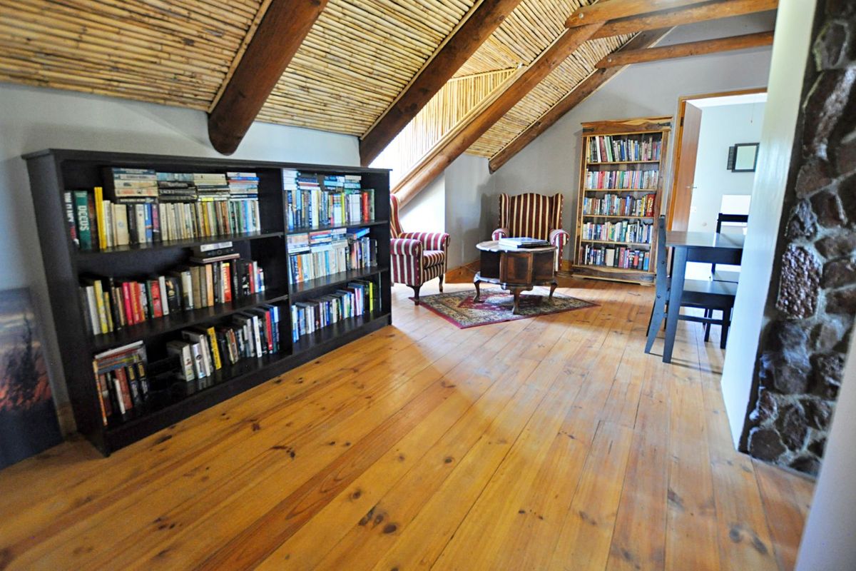 Attic-style living area featuring exposed timber beams, bamboo ceiling paneling, and polished wooden flooring with a stone feature wall.