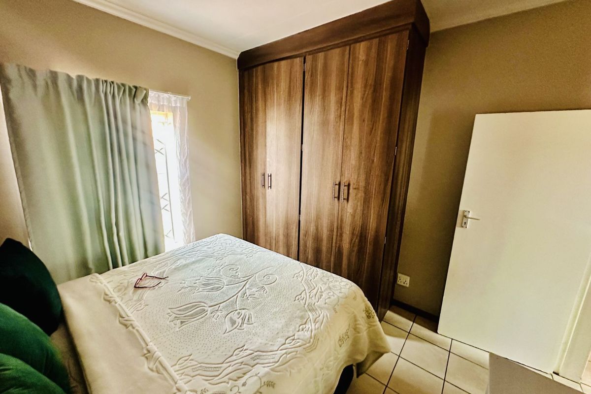 A bedroom featuring built-in wooden cupboards, tiled flooring, and a window with curtaining.