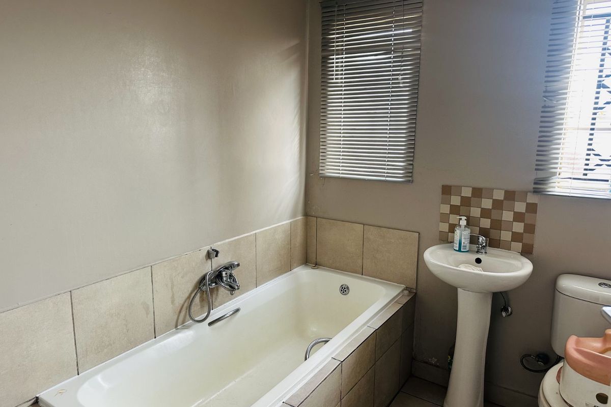 A functional bathroom featuring a built-in bathtub with shower mixer, pedestal basin, and tiled splashbacks.