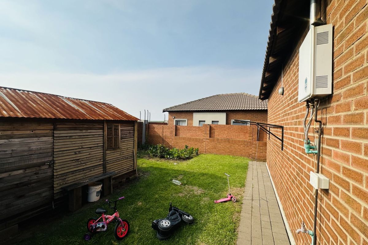 Rear garden area featuring a brick boundary wall, a paved walkway, and a wooden storage shed with a corrugated metal roof.
