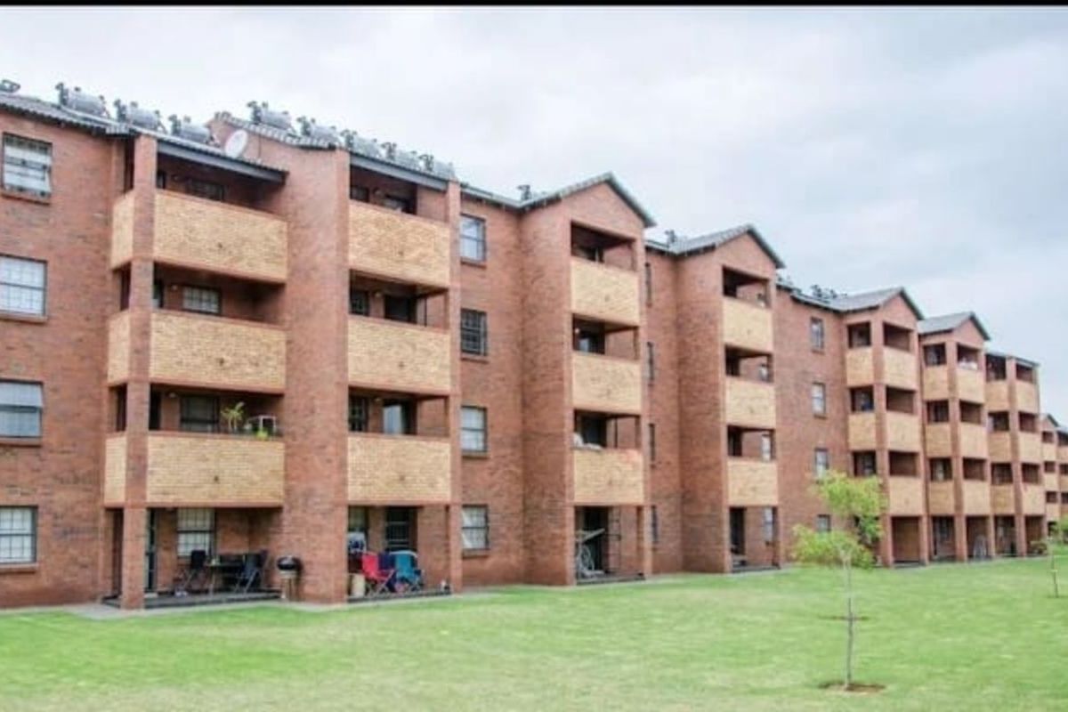 Exterior view of a multi-story brick apartment complex featuring private balconies and a shared lawn area.