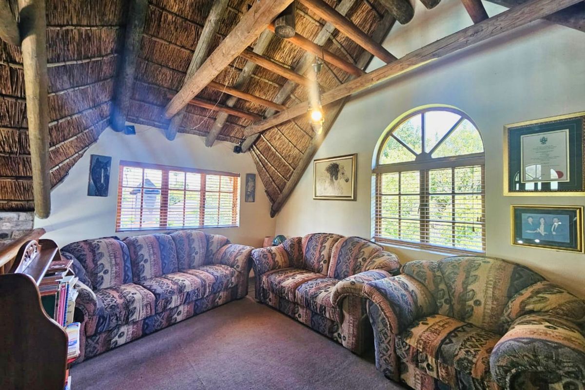 A cozy living room featuring a high vaulted thatched ceiling with exposed timber beams, arched windows, and carpeted flooring.
