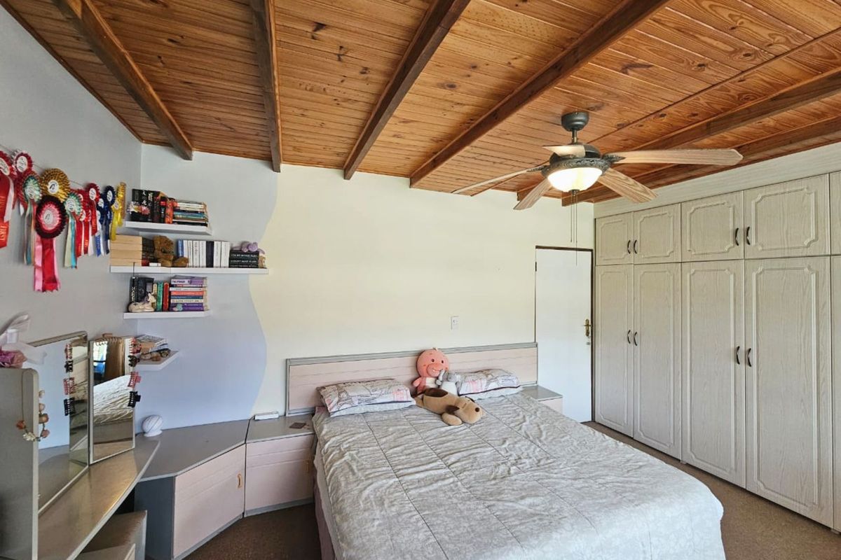 A bedroom featuring a timber-beamed ceiling, built-in wardrobes, and integrated bedside cabinetry with shelving.