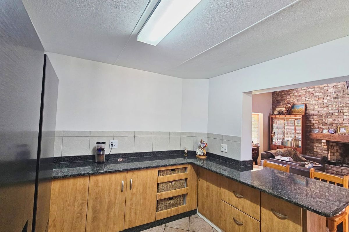 A functional kitchen featuring granite countertops, wooden cabinetry, and tiled flooring, with an open-plan layout connecting to the adjacent living area.