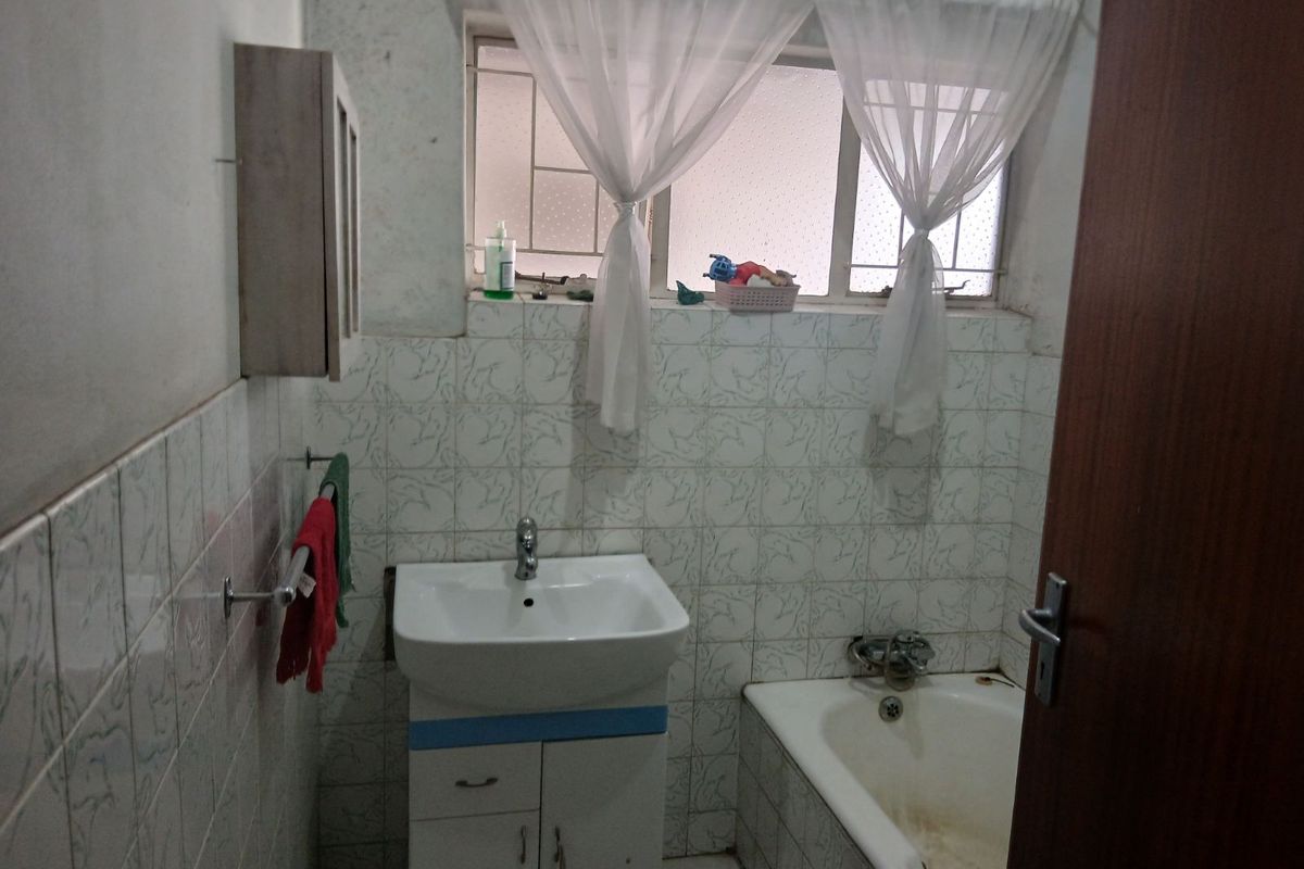 A dated bathroom featuring a bathtub, pedestal basin, and tiled walls. The space requires renovation to update the finishes and fixtures.