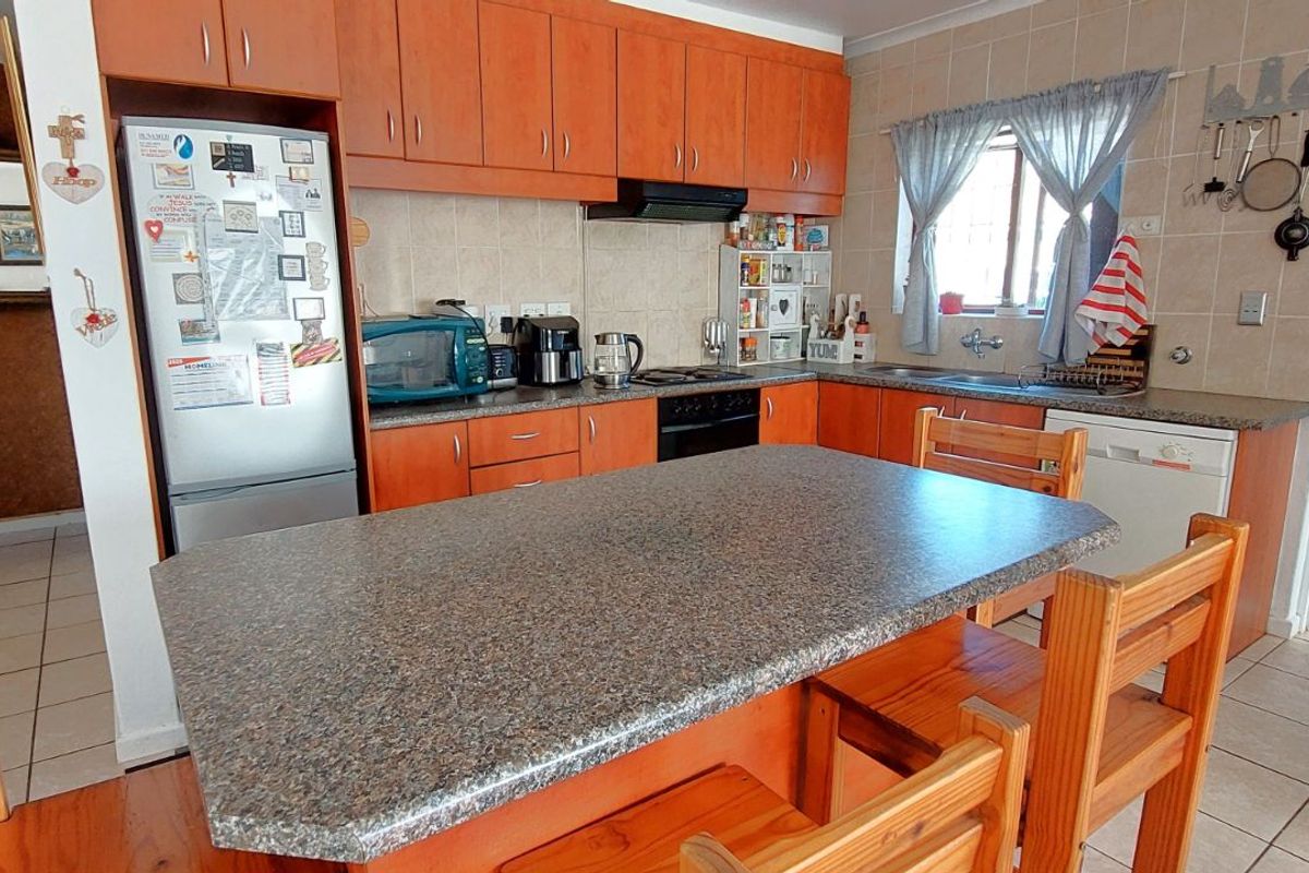 Functional kitchen featuring wooden cabinetry, granite-look countertops, a central breakfast island, and tiled flooring with an adjacent utility area.