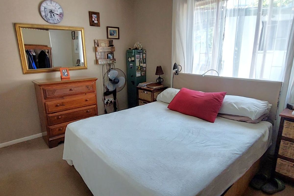 A functional bedroom featuring neutral wall tones, carpeted flooring, and a large window allowing for natural light.