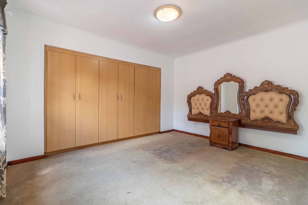 A bedroom featuring built-in wooden wardrobes and a wall-mounted vanity unit, finished with neutral walls and carpeted flooring.