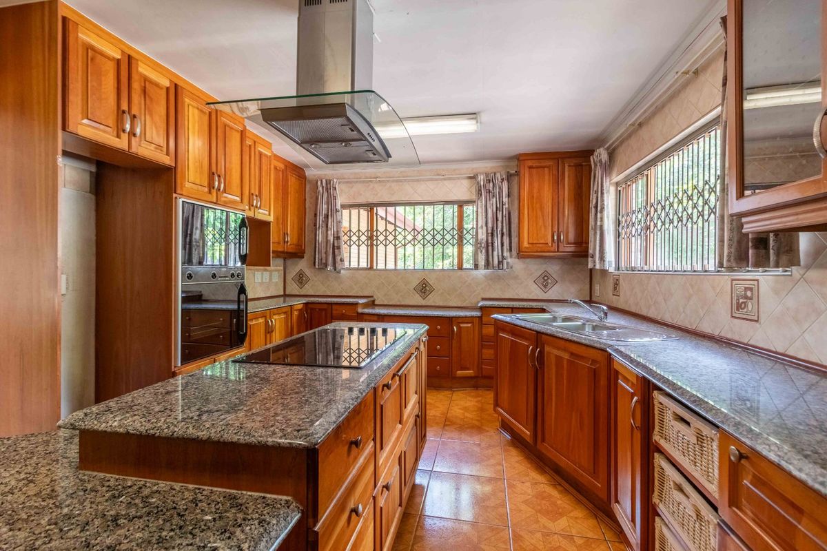 A traditional kitchen featuring warm-toned wooden cabinetry, granite countertops, a central island with a built-in hob, and a stainless steel extractor fan.