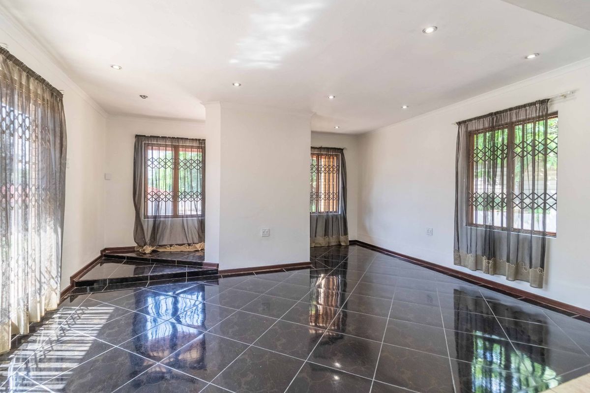 Spacious living area featuring polished dark ceramic floor tiles, recessed ceiling lighting, and security gates on windows.