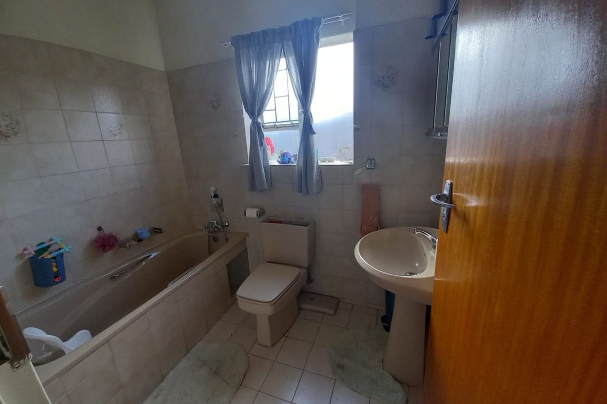 A dated bathroom featuring a built-in bathtub, pedestal basin, and toilet with neutral wall and floor tiling.