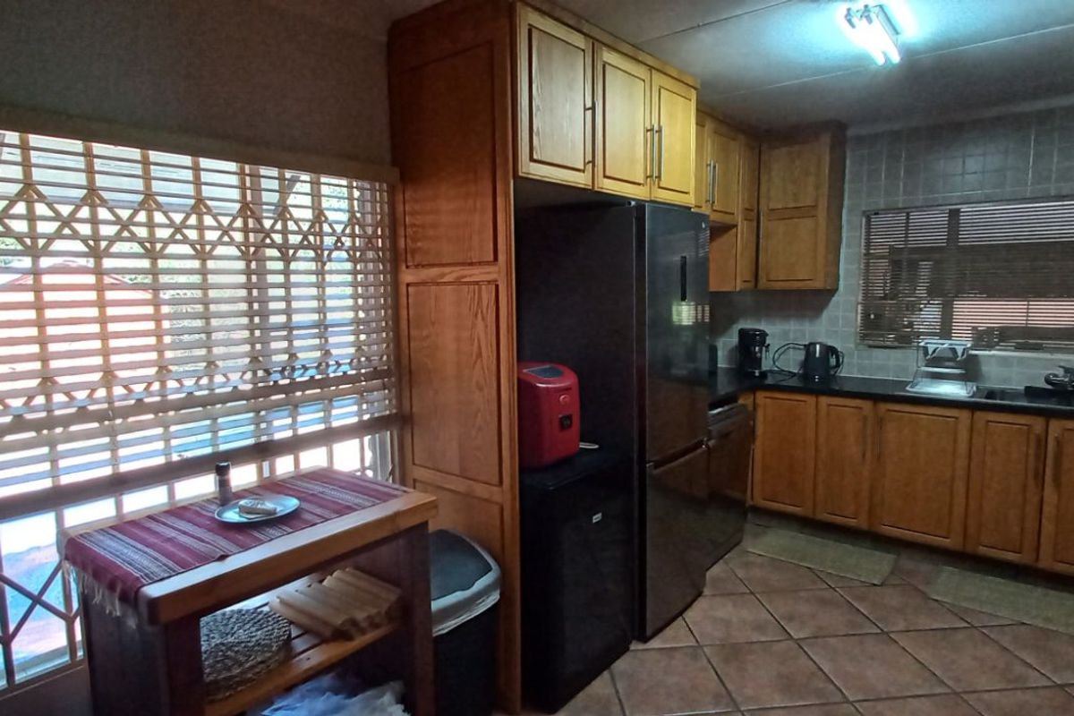 A functional kitchen featuring wooden cabinetry, dark countertops, tiled flooring, and a large window with security shutters.