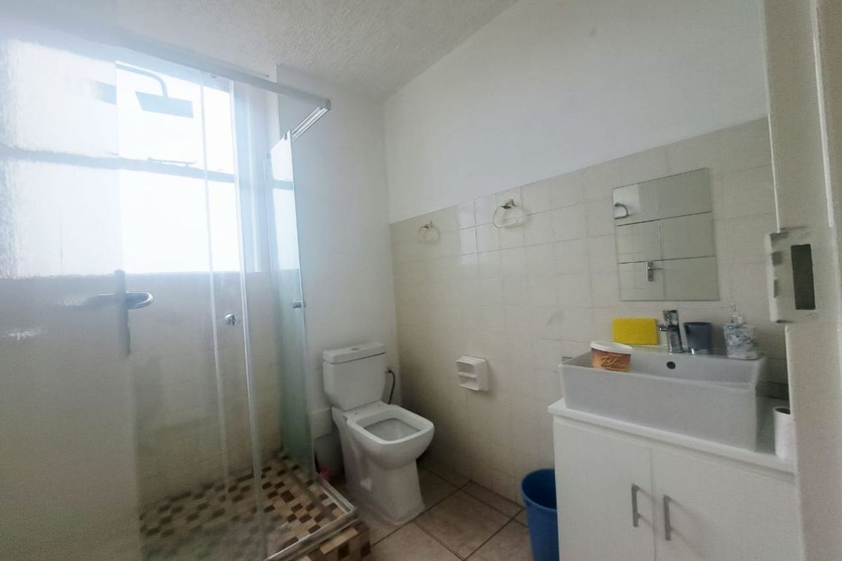 A functional bathroom featuring a glass-enclosed shower, a modern vanity basin, and a standard toilet with tiled flooring and wall finishes.