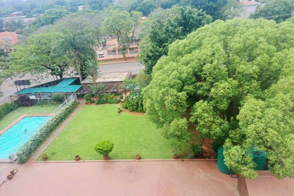 Elevated aerial view overlooking a lush garden, swimming pool, and surrounding neighborhood greenery.