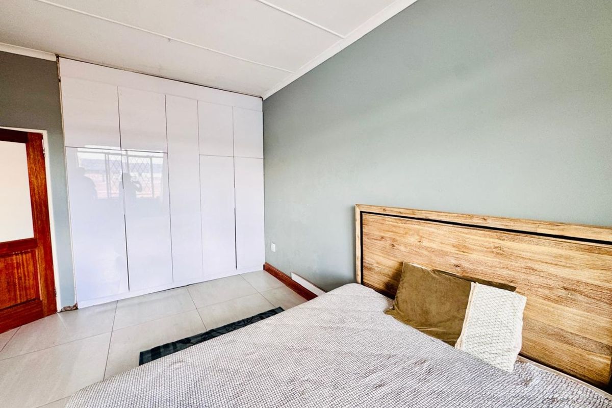 A well-lit bedroom featuring modern white built-in cupboards, neutral wall tones, and tiled flooring, providing a clean and functional living space.