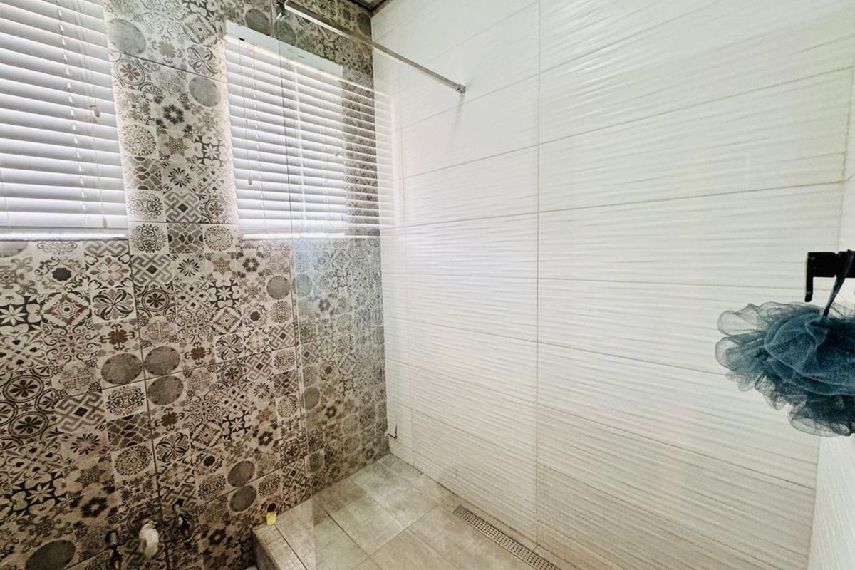 A modern walk-in shower featuring decorative patterned wall tiles, textured white wall tiles, a linear floor drain, and a glass shower screen.