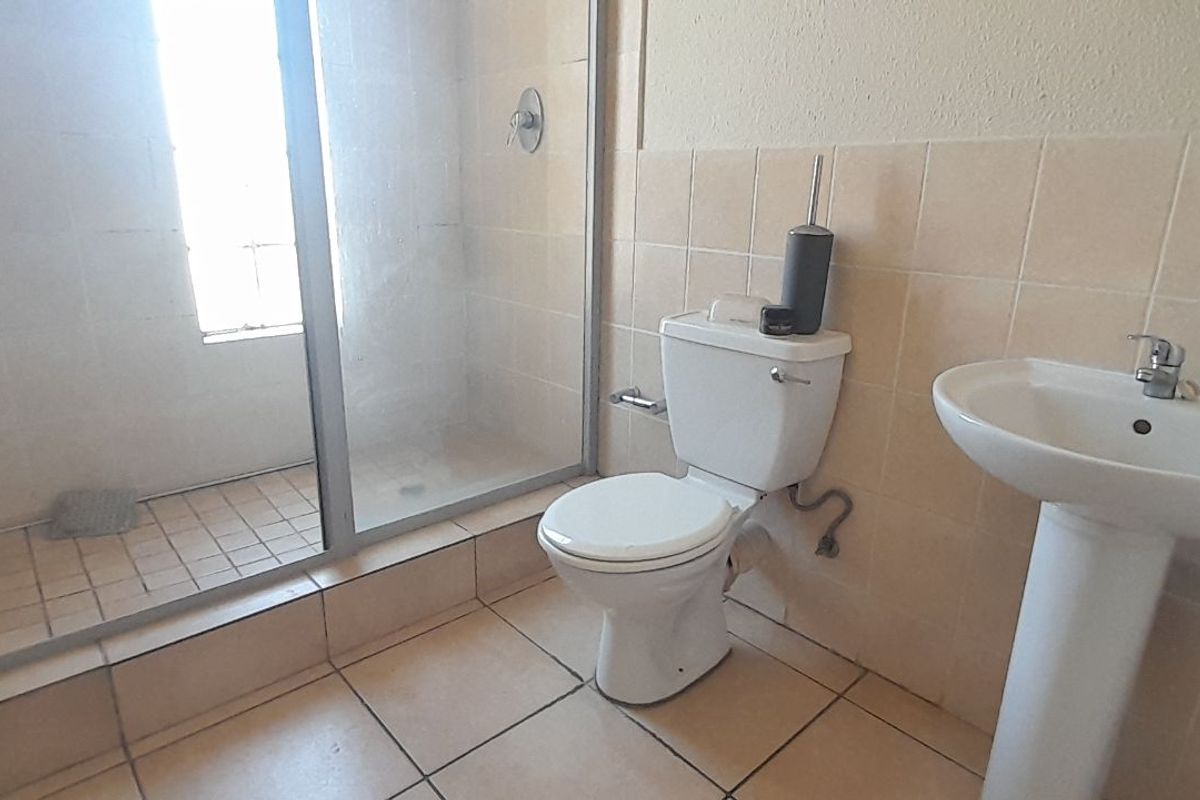 A functional bathroom featuring a glass-enclosed shower, a pedestal basin, and a standard toilet with neutral wall and floor tiling.