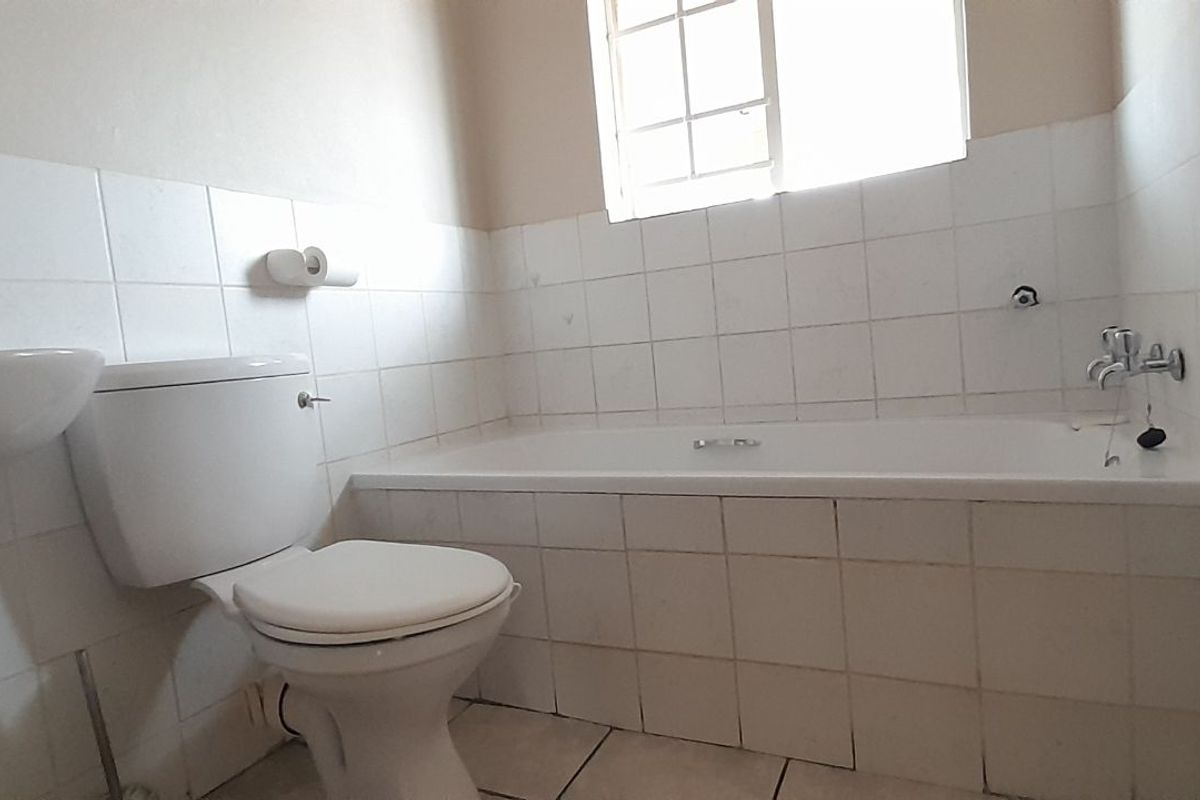 A functional bathroom featuring a white pedestal basin, a standard toilet, and a tiled bathtub with a window for natural light.