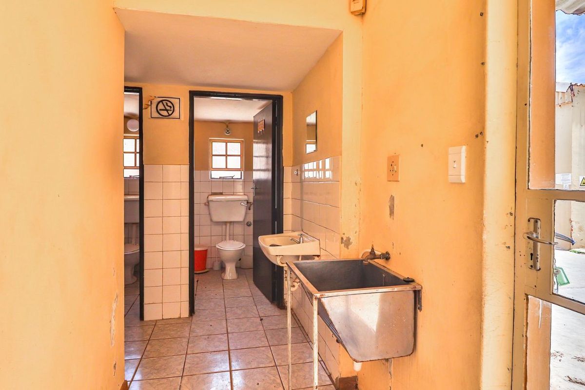 A functional industrial washroom area featuring tiled walls, multiple toilet cubicles, and a stainless steel utility sink.