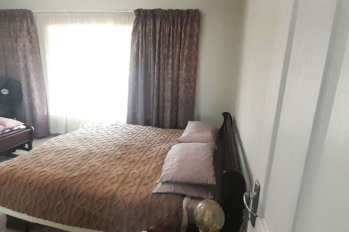 A bedroom featuring tiled flooring and a large window with curtains, providing natural light to the space.