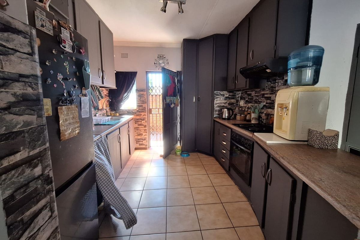 A functional galley-style kitchen featuring dark cabinetry, stone-effect backsplash tiling, ceramic floor tiles, and a built-in oven with extractor fan.