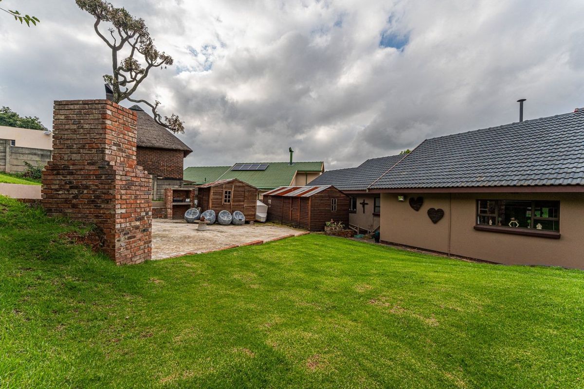 A spacious rear garden featuring a paved patio area with a built-in brick fireplace, lawn, and multiple wooden storage structures.