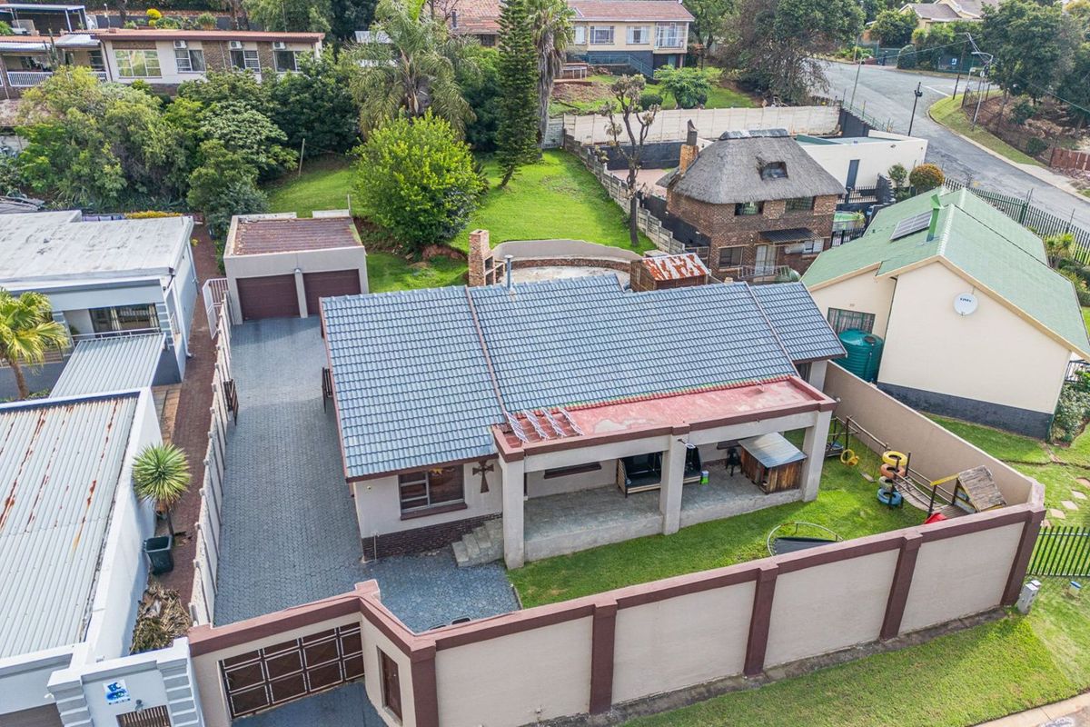 Aerial view of a residential property featuring a tiled roof, paved driveway, double garage, and a covered patio area within a walled garden.