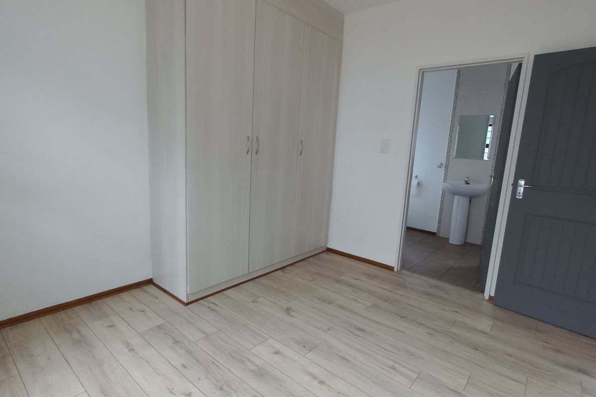 A bright bedroom featuring light wood-look laminate flooring, built-in cupboards, and direct access to an en-suite bathroom.