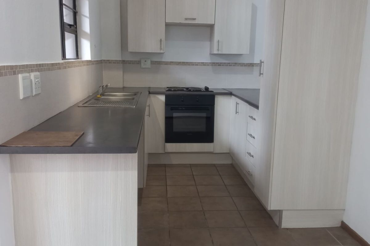 A functional kitchen featuring light wood-grain cabinetry, dark countertops, a built-in oven, hob, and tiled flooring.