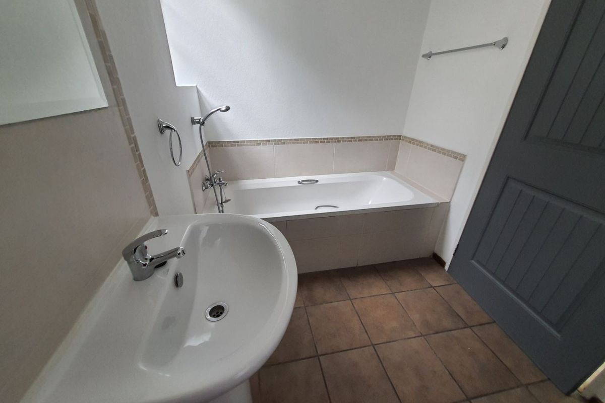 A functional bathroom featuring a white pedestal basin, a built-in bathtub with shower mixer, and tiled flooring.