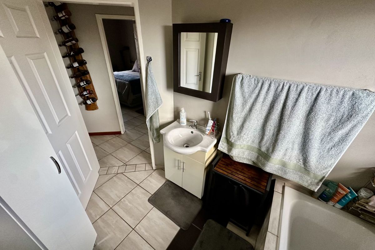 A functional bathroom featuring a vanity with a basin, a wall-mounted mirror, and tiled flooring, with a view into the adjacent bedroom.