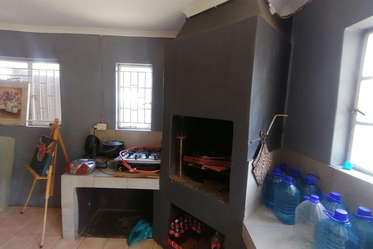 An indoor entertainment area featuring a built-in braai fireplace, tiled flooring, and a masonry prep counter with a gas hob.