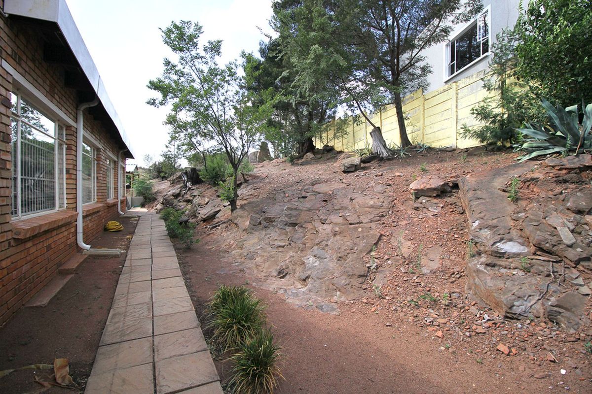 A side exterior view of the property featuring a paved walkway alongside a natural rocky slope and a boundary wall.