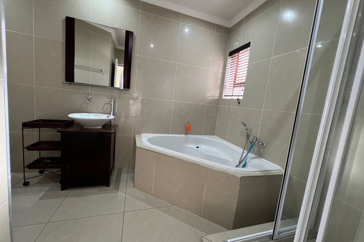 A modern bathroom featuring a corner bathtub, a vessel sink vanity with a wall-mounted mirror, and neutral floor-to-ceiling wall tiles.