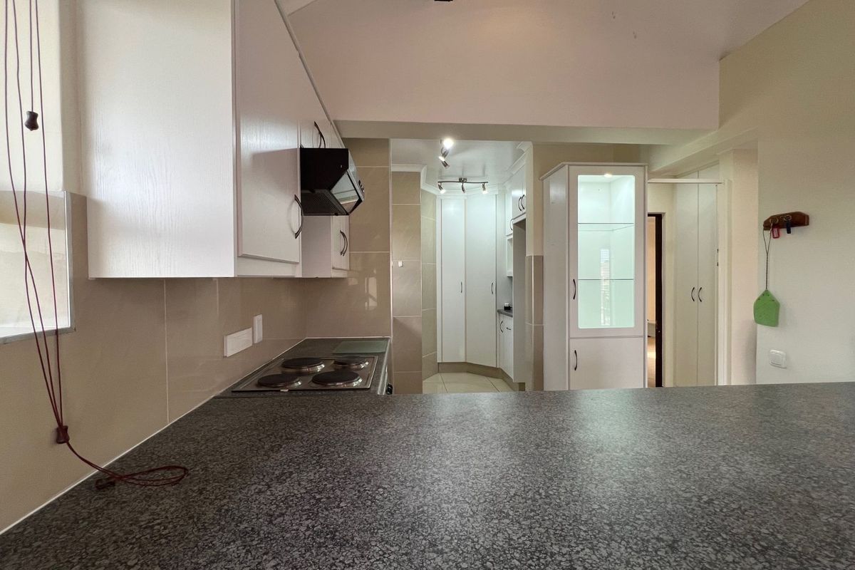 A functional kitchen featuring granite countertops, built-in cabinetry, an integrated hob, and an extractor fan, with an open-plan layout leading to adjacent living areas.