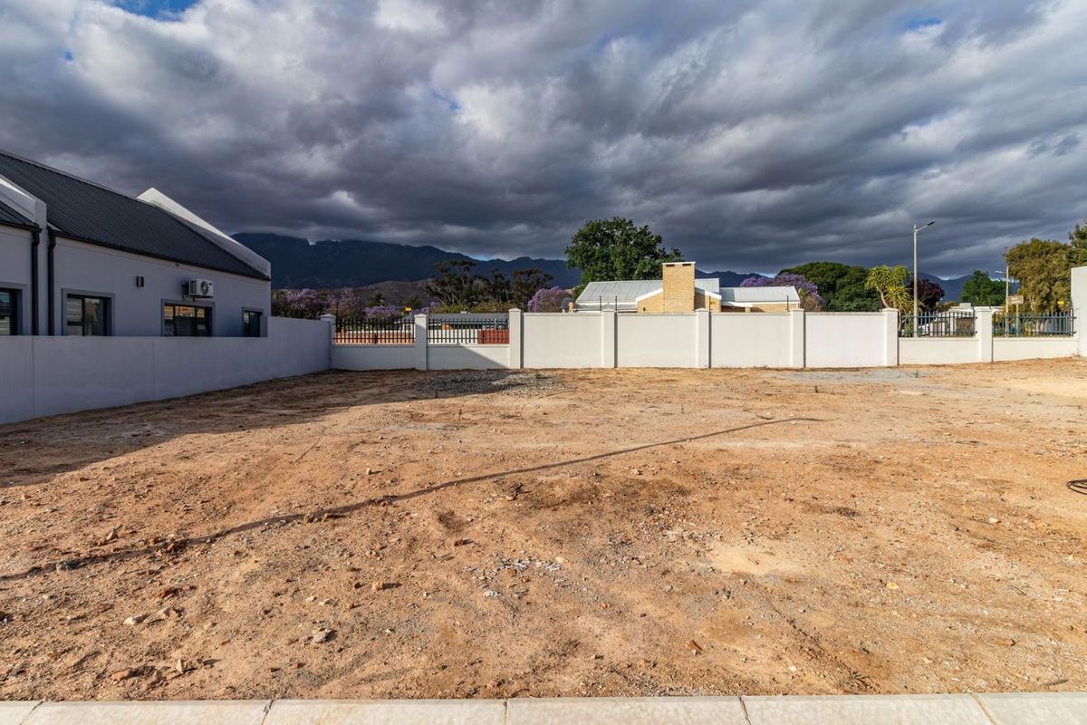 A vacant residential plot featuring perimeter boundary walls and clear views of the surrounding landscape and mountains.