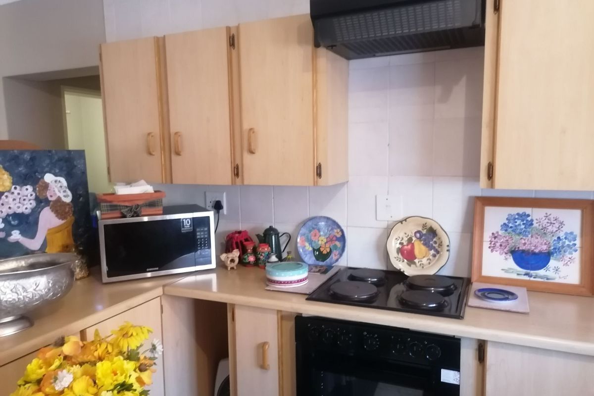 A functional kitchen featuring light wood-tone cabinetry, a built-in electric oven, a black ceramic hob, and an overhead extractor fan.