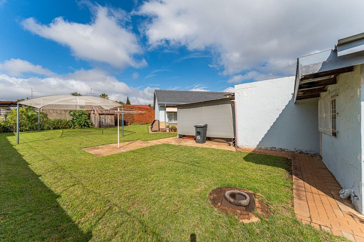 A spacious rear garden featuring a lawn area, paved pathways, and a covered outdoor structure, providing ample space for outdoor activities.