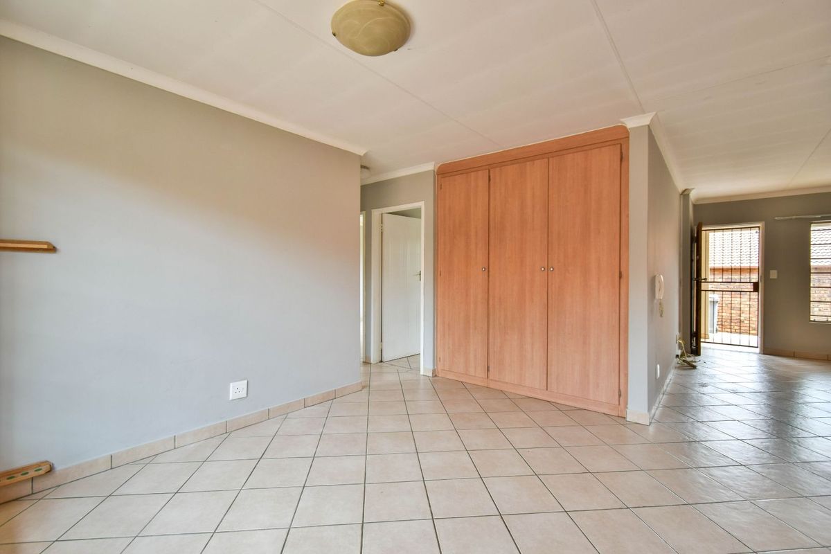 A bright, empty bedroom featuring neutral walls, tiled flooring, and built-in wooden cupboards, providing a clean and versatile living space.