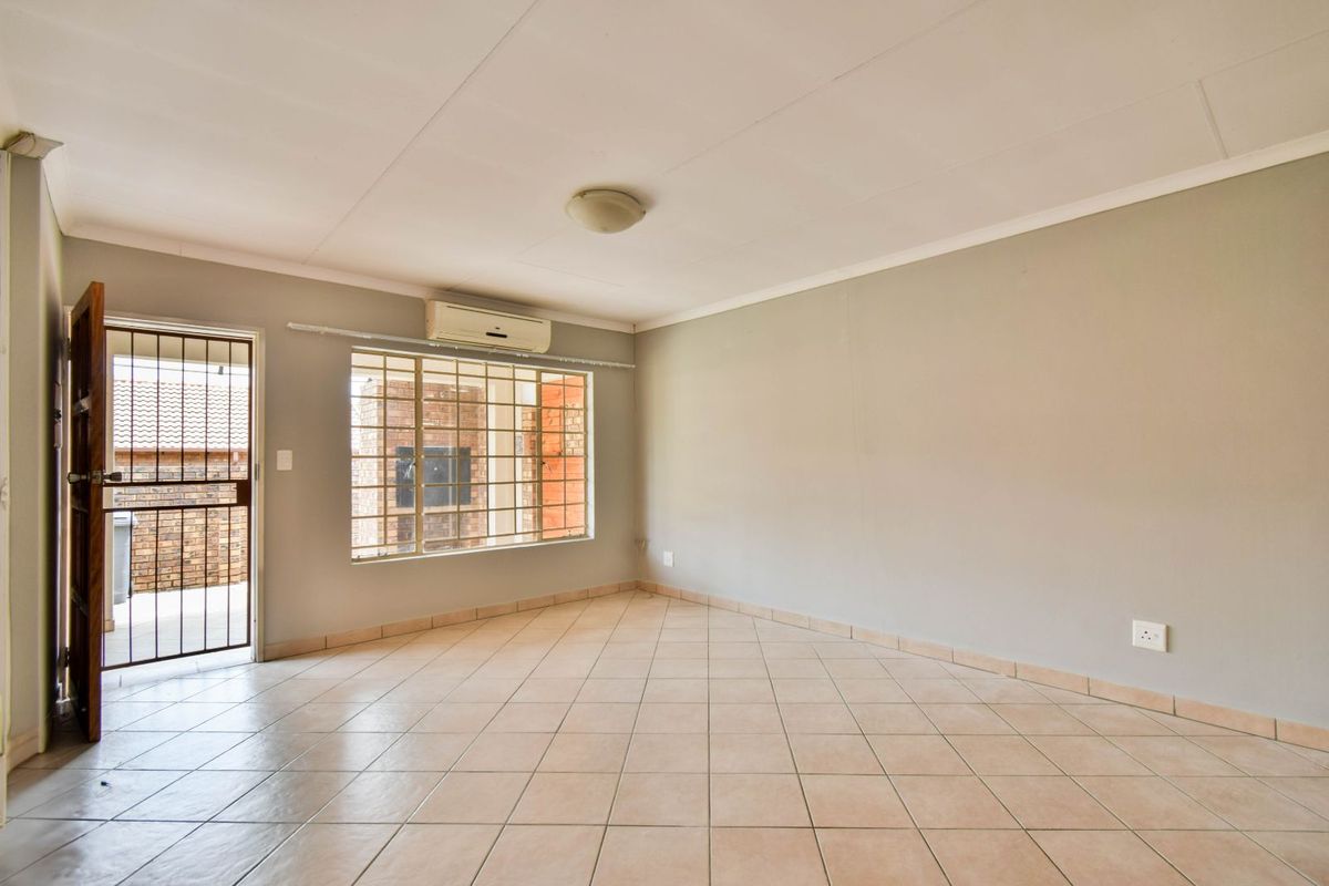 A bright, empty living room featuring neutral tiled flooring, a wall-mounted air conditioning unit, and a security gate at the entrance.