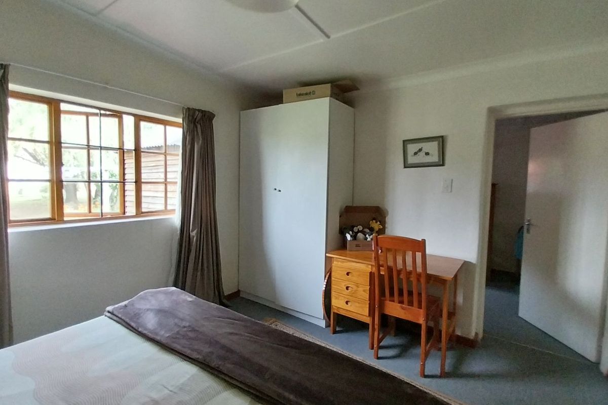 A functional bedroom featuring a built-in wardrobe, large window with natural light, and neutral wall finishes.