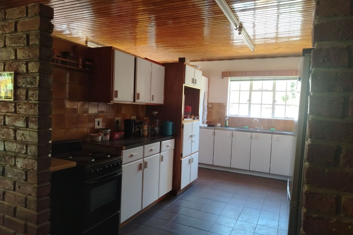 A functional kitchen featuring tiled flooring, timber ceiling, and ample built-in cabinetry with a freestanding stove and double sink.