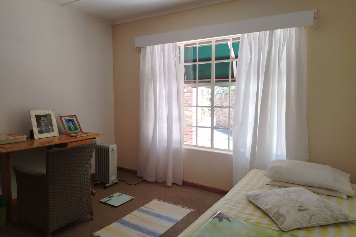 A functional bedroom featuring carpeted flooring, a large window with exterior security bars, and neutral wall finishes.