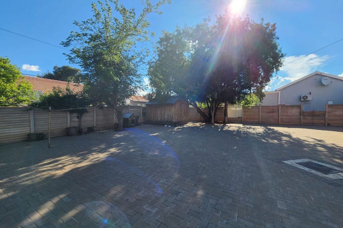 A spacious paved backyard featuring perimeter fencing, mature trees, and a wooden storage shed, offering a low-maintenance outdoor area.