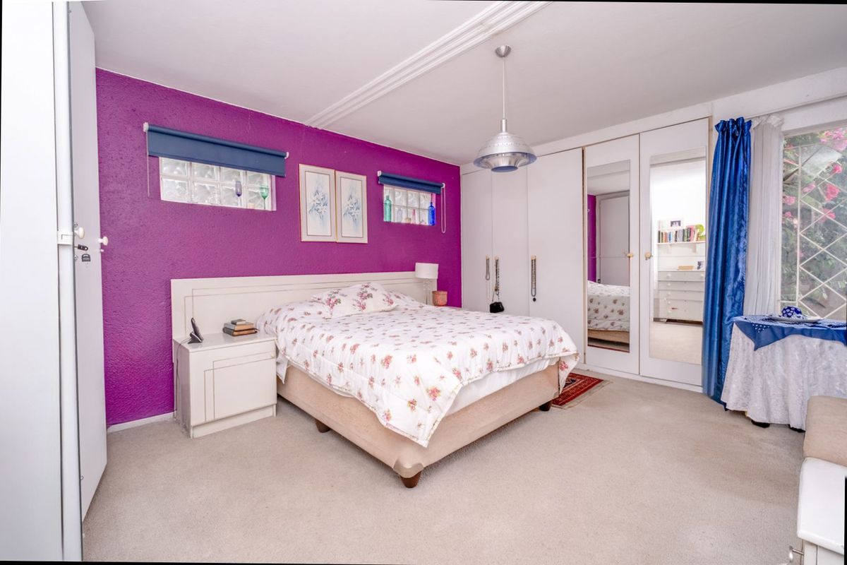 A bedroom featuring built-in wardrobes with mirrored panels, glass block windows, and a prominent purple accent wall.