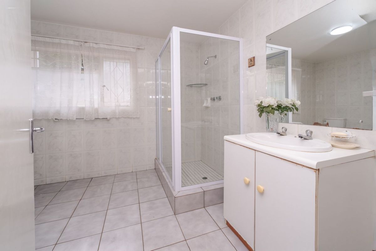 A functional bathroom featuring a glass-enclosed shower, a single vanity with integrated basin, and tiled flooring and walls.