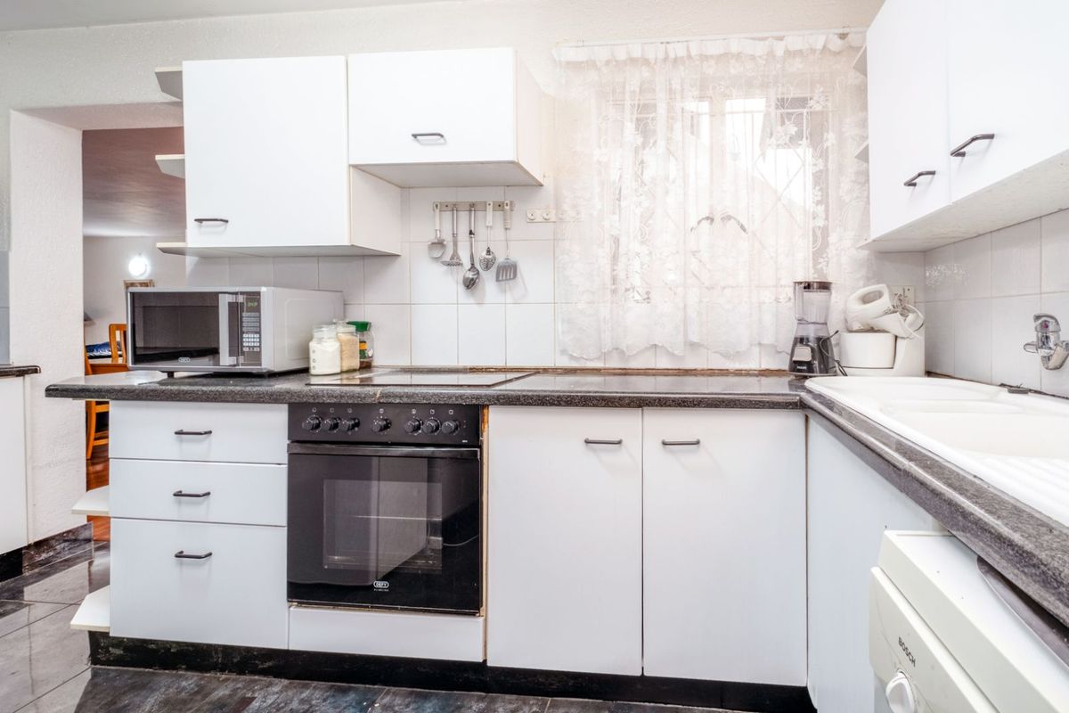 A functional kitchen featuring white cabinetry, dark countertops, a built-in oven, and a tiled backsplash with a window view.
