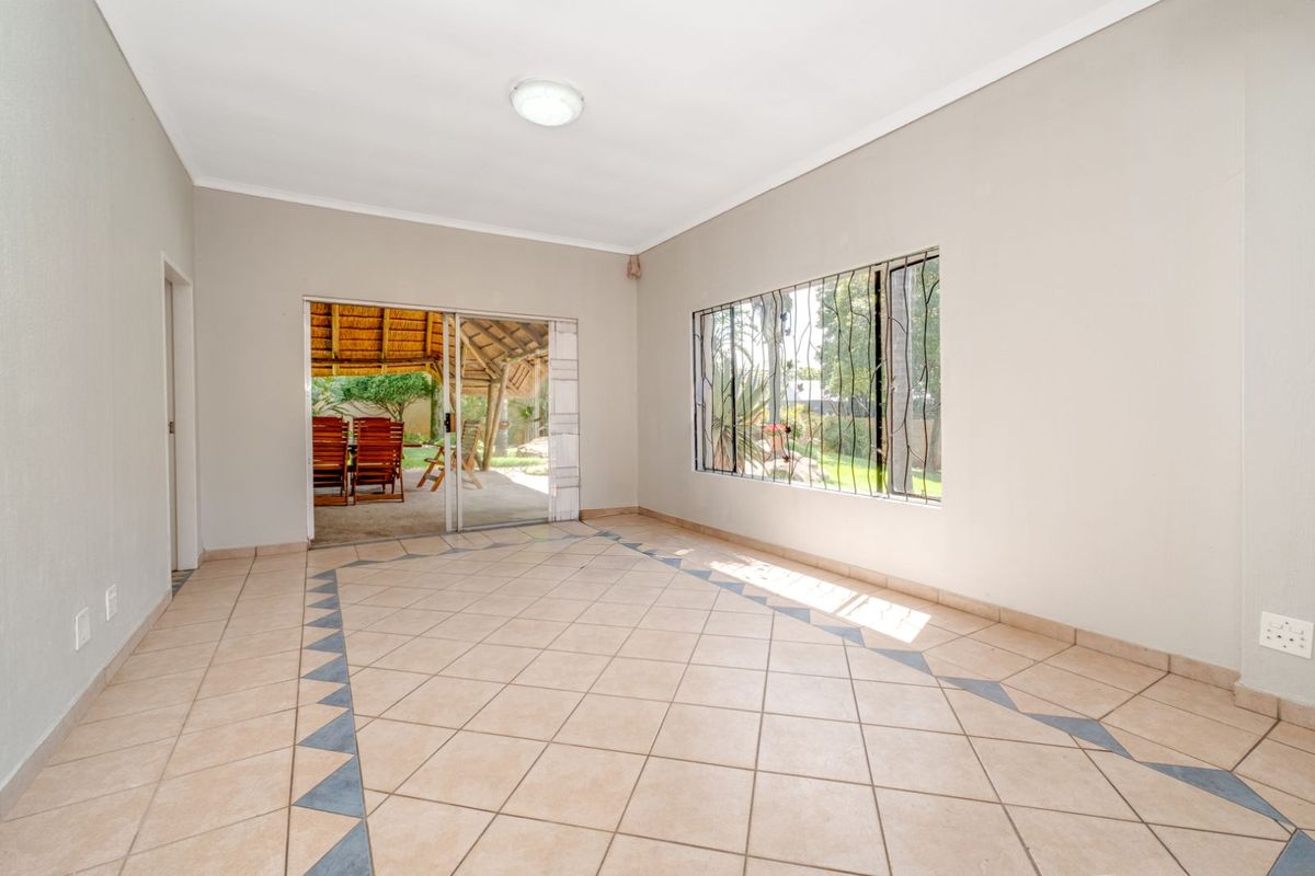 A bright, empty living area featuring tiled flooring, large windows with security bars, and sliding glass doors leading to an outdoor patio space.